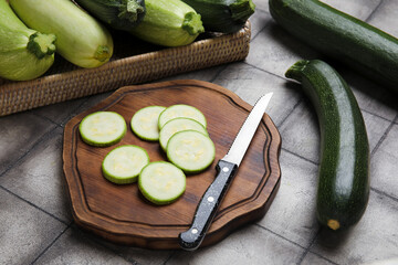 Wooden board with slices of fresh zucchini on black tile background