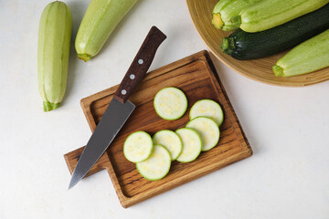 Wooden board with slices of fresh zucchini on light background