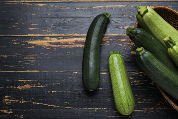 Wicker bowl with fresh green zucchini on black wooden background