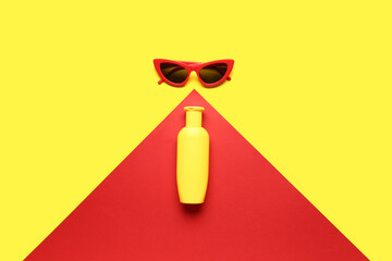 Sunglasses with bottle of sunscreen cream on color background