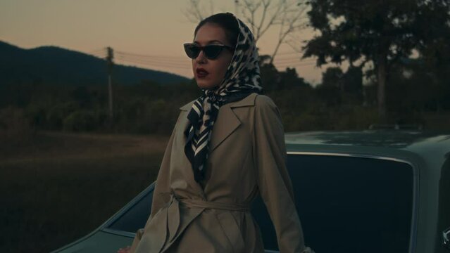 Attractive young elegant woman in a retro outfit sits on the hood of her car. 