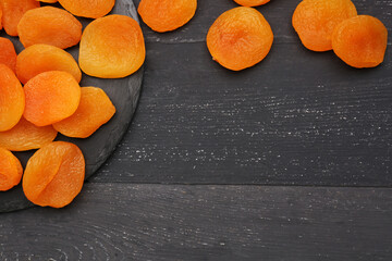 Board with tasty dried apricots on black wooden background