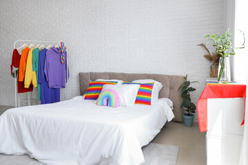 Interior of light bedroom with rainbow pillows, clothes and LGBT flag