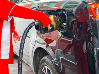 gas station worker's hand in red uniform holding fuel pump nozzle and refueling in diesel car. biodiesel fuel in Indonesia