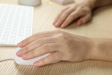 Woman using wired computer mouse at wooden table, closeup