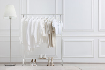 Rack with different stylish women`s clothes, shoes and lamp near white wall indoors, space for text