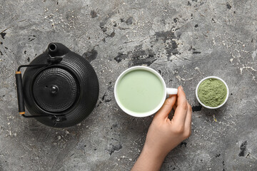 Female hand with cup of fresh matcha tea, powder and teapot on grunge background