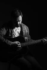 Black and white portrait of a caucasian man playing an acoustic guitar. He is in his 40s and is...