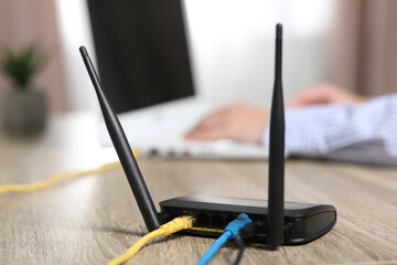 Woman working with laptop at table indoors, focus on Wi-Fi router