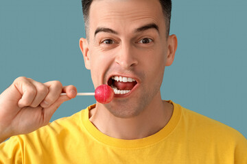 Handsome man eating lollipop on blue background, closeup