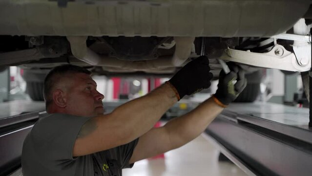 Auto mechanic adjusts vehicle wheel alignment at modern auto repair shop. Professional uses equipment for accuracy, ensures car safety and efficiency. Service technician works under lifted car.