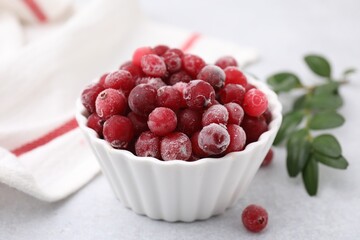 Frozen red cranberries in bowl and green leaves on light table, closeup