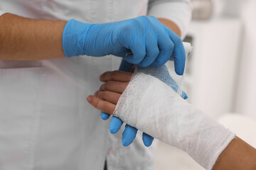 Doctor bandaging patient's burned hand indoors, closeup
