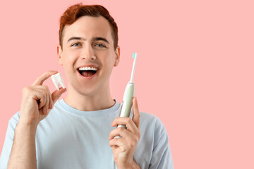 Young man with plastic teeth and electric toothbrush on pink background, closeup - obrazy, fototapety, plakaty