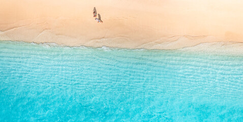 Aerial view of amazing beach with couple walking in sunset light close to turquoise sea. Top view of summer beach landscape, romantic love couple vacation, romantic holiday. Freedom leisure activity
