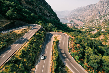 Car drives along a serpentine highway in the mountains overlooking the Bay of Kotor. Montenegro. Drone