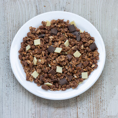 Delicious granola with oatmeal and chocolate chips in a white plate on a wooden surface