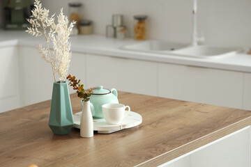 Wooden table with tea set, dried flowers and eucalyptus branches in modern kitchen, closeup