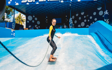 Beautiful young woman surfing with trainer on a wave simulator at a water amusement park