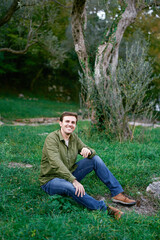 Naklejka na ściany i meble Young man sitting on green grass near the tree
