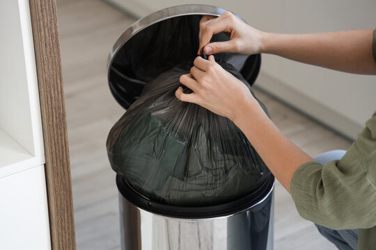 Woman throwing full garbage bug into trash bin in kitchen, closeup