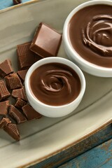 Bowls of tasty melted chocolate on blue wooden background