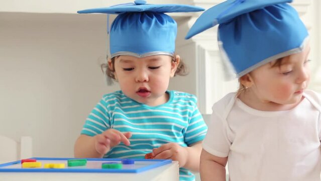Two cute babies in graduation hats play with letters on magnets