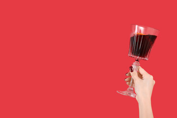 Female hand with glass of warm mulled wine on red background