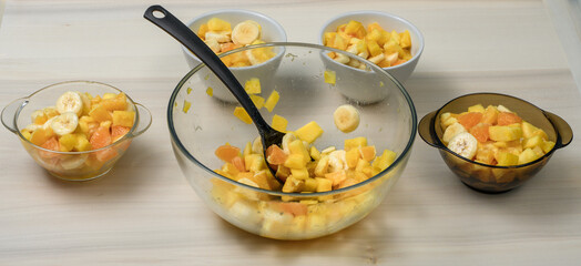 Owoce pokrojone na kawałki jak banan, pomarańcza i ananas nakładane do miseczek, dużo owoców...