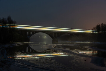 Fototapeta na wymiar Night Train Crossing Illuminated Bridge over Water at Dusk