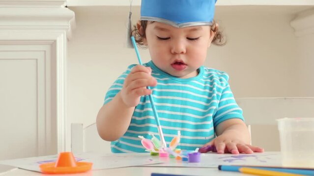 Two cute baby boy in blue graduation hat paints colors on table