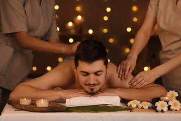 Obraz na płótnie Canvas Young man getting massage from therapists in dark spa salon