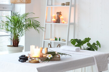 Spa composition with burning candles and plumeria flowers on couch in light salon