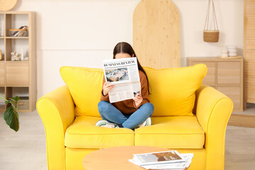 Young woman reading newspaper on sofa at home