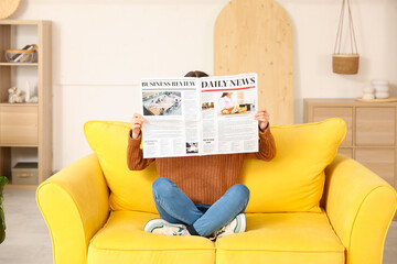 Young woman reading newspaper on sofa at home