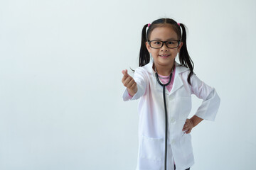 Girl wearing doctor's uniform and glasses standing smiling playing doctor showing hand gesture of...