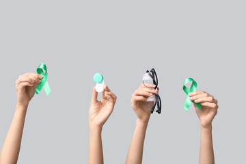 Female hands with container for contact lenses, green ribbons and eyeglasses on grey background....