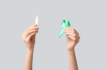 Female hands with green ribbon and eye drops on grey background. Glaucoma awareness concept