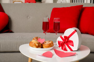 Heart-shaped gift box, glasses of wine and sweet buns on coffee table in living room. Valentine's Day celebration