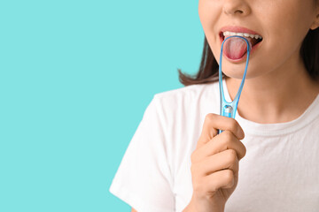 Young woman using tongue scraper on blue background, closeup