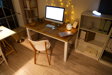 Interior of office with workplace, shelf units and glowing lights at night