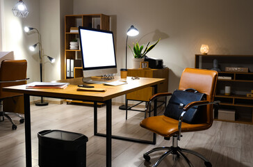 Modern workplace with computer and briefcase on chair in office at night