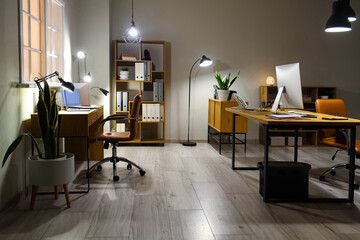 Interior of modern office with desks and glowing lamps - obrazy, fototapety, plakaty