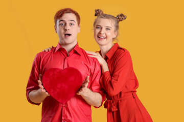 Young couple with gift box on yellow background. Valentine's Day celebration