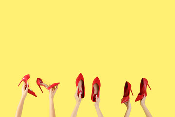 Fototapeta premium Female hands holding stylish red shoes on yellow background
