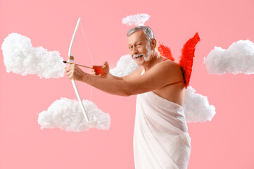 Mature man dressed as Cupid shooting bow in clouds on pink background. Valentine's Day celebration