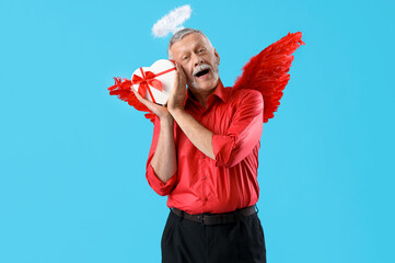 Mature man dressed as Cupid with gift box on blue background. Valentine's Day celebration