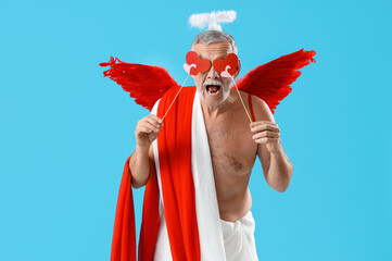 Mature man dressed as Cupid with hearts on blue background. Valentine's Day celebration