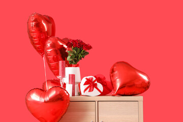 Wooden chest of drawers with heart-shaped air balloons, roses, candles and gifts on red background....