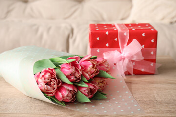 Tulips with gift box on table in living room, closeup. International Women's Day celebration